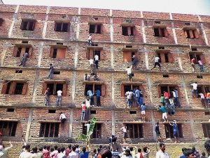 Vaishali: Youths climbing the building of an examination centre to help the candidates in cheating, by passing notes through the windows, during a Matriculation examination in Hajipur, on Wednesday. 